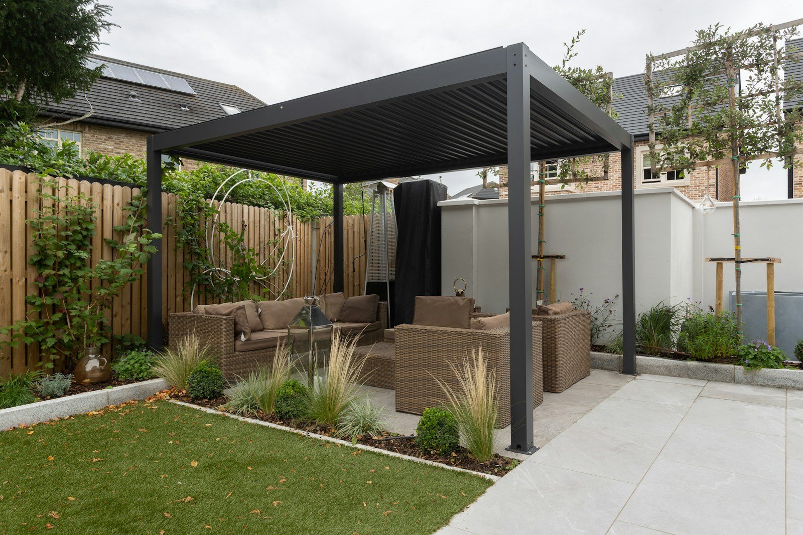 Pérgola de lamas oscuras con zona de estar en un jardín como referencia para pérgolas